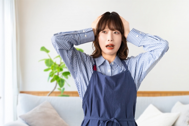 頭を抱えて悩むエプロン姿の女性